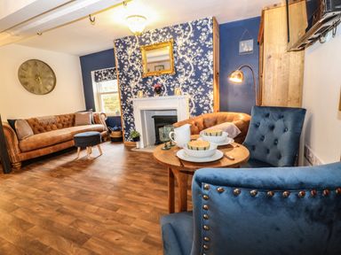 A living room with two brown sofas a round wooden table set for two and a fireplace at The Cheese Room in Stretton-On-Fosse