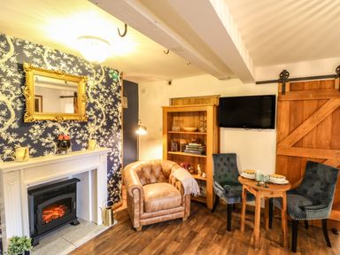 A room with a fireplace armchair bookshelf wall-mounted tv dining table with two chairs and sliding wooden door at The Cheese Room in Stretton-On-Fosse