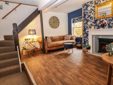 A living room with a brown sofa and blue ottoman near a fireplace and staircase at The Cheese Room in Stretton-On-Fosse