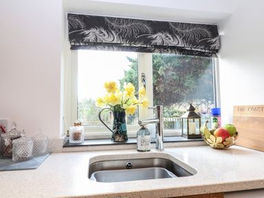 A kitchen sink with a faucet under a window with flowers soap and fruit bowl on the counter at The Cheese Room in Stretton-On-Fosse