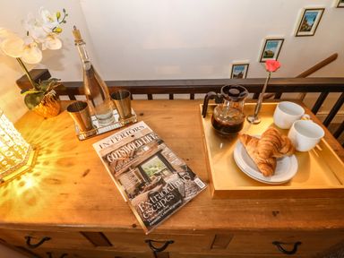 A wooden table with a coffee pot croissant cups a bottle with two metal cups a magazine and a small flower vase at The Cheese Room in Stretton-On-Fosse
