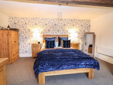 A bedroom with a wooden bed blue bedding two wooden nightstands with lamps a wooden wardrobe and a standing mirror at The Cheese Room in Stretton-On-Fosse