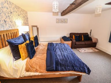 A bedroom with a wooden bed with pillows and blankets a brown sofa with cushions a wooden nightstand with folded towels and framed pictures on the wall at The Cheese Room in Stretton-On-Fosse