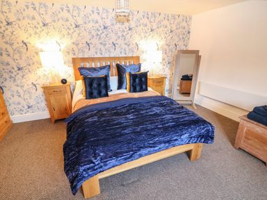 A bedroom with a wooden bed blue bedding two bedside tables with lamps a full length mirror and patterned wallpaper at The Cheese Room in Stretton-On-Fosse