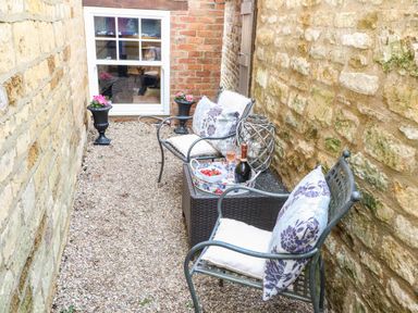 A small outdoor seating area with two chairs and a table between stone walls at The Cheese Room in Stretton-On-Fosse