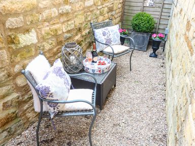 A small outdoor seating area with two metal chairs with cushions and a small table with a tray of strawberries and drinks at The Cheese Room in Stretton-On-Fosse