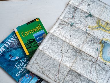 An unfolded map and two Cornwall guidebooks on a white surface