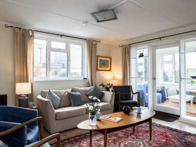 A living room with a beige sofa blue chairs a wooden coffee table and glass doors leading to a sunroom at Croft Elms in Trebetherick near Polzeath
