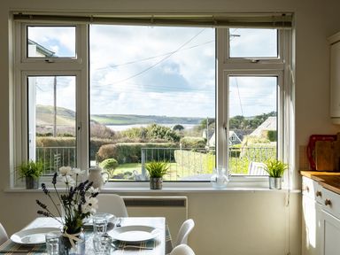 A dining area with a table set with plates and glasses in front of a window showing a garden and hills at Croft Elms in Trebetherick near Polzeath