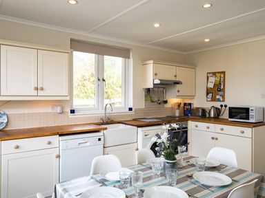 A kitchen with white cabinets wooden countertops a dining table set with plates glasses and cutlery and a window at Croft Elms in Trebetherick near Polzeath