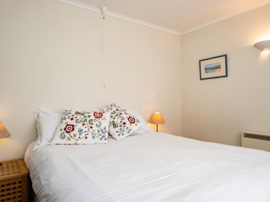 A bedroom with a double bed and floral pillows with bedside tables and lamps at Croft Elms in Trebetherick near Polzeath
