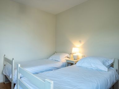 A room with two single beds and a lit lamp on a small table between them at Croft Elms in Trebetherick near Polzeath