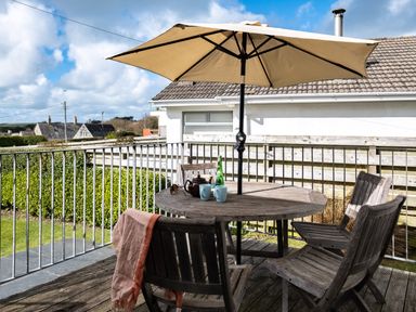 A wooden patio table with chairs and an umbrella on a balcony overlooking a garden at Croft Elms in Trebetherick near Polzeath