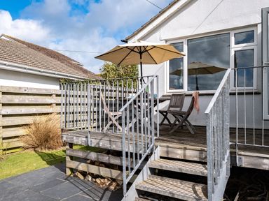 An outdoor wooden deck with metal railing and steps two wooden chairs and a table with an umbrella at Croft Elms in Trebetherick near Polzeath
