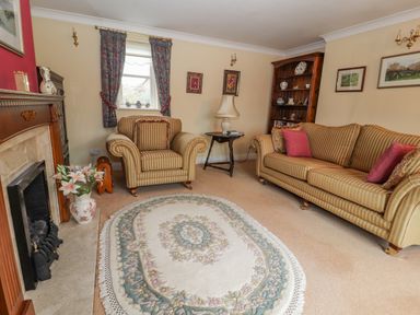 A living room with striped sofa and armchair a floral rug a fireplace and a wooden bookshelf at Bryn Offa cottage in Holywell