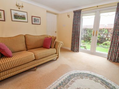 A living room with a striped sofa and red cushions near glass doors with floral curtains at Bryn Offa cottage in Holywell