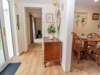 A hallway with a wooden sideboard and floral arrangement leading to a living room and a dining area with a wooden table and chairs at Bryn Offa cottage in Holywell