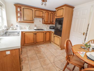 A kitchen with wooden cabinets a sink a gas stove an oven and a wooden dining table with chairs at Bryn Offa cottage in Holywell