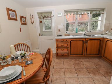 A kitchen with wooden cabinets a round dining table set with dishes and glasses at Bryn Offa cottage in Holywell