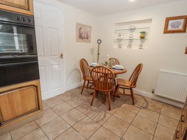 A dining area with a round wooden table and four chairs set with dishes in a kitchen at Bryn Offa cottage in Holywell