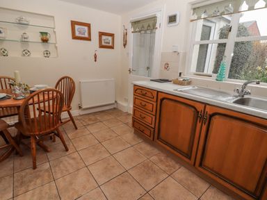 A kitchen with wooden cabinets a sink a window and a dining table with chairs at Bryn Offa cottage in Holywell
