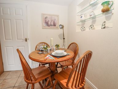 A dining area with a round wooden table set for four with wooden chairs a floor lamp and shelves with decorative items at Bryn Offa cottage in Holywell
