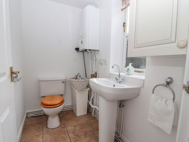 A small bathroom with a toilet with a wooden seat a white sink a towel ring with a white towel and a window at Bryn Offa cottage in Holywell