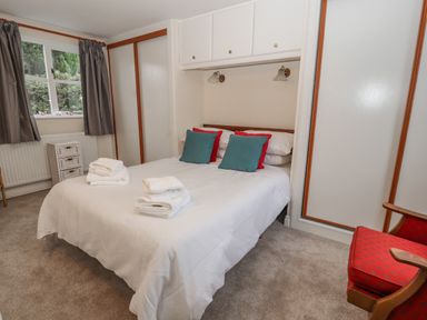 A bedroom with a double bed with folded towels and pillows two wardrobes a window with curtains and a red chair at Bryn Offa cottage in Holywell