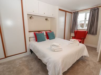 A bedroom with a bed with folded towels and pillows and a red armchair by the window at Bryn Offa cottage in Holywell