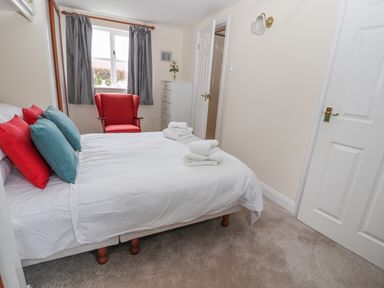A bedroom with a bed with red and blue pillows a red armchair gray curtains and a white dresser at Bryn Offa cottage in Holywell