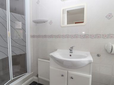 A bathroom with a sink vanity unit a mirror shower enclosure and tiled walls at Bryn Offa cottage in Holywell