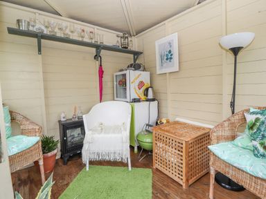 A small room with wicker chairs and a white armchair around a wooden table with a green rug on the floor at Bryn Offa cottage in Holywell
