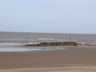 A sandy beach with a rock jetty and a green navigation marker at Bryn Offa cottage in Holywell