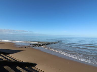 A sandy beach with a rocky outcrop extending into calm sea water under a clear blue sky at Bryn Offa cottage in Holywell