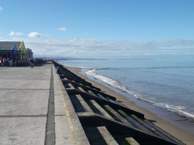 A coastal promenade with a concrete sea wall and people walking near colorful buildings at Bryn Offa cottage in Holywell
