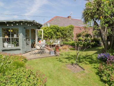 A garden with a small patio area and table with chairs and a wooden summerhouse at Bryn Offa cottage in Holywell