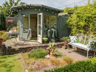 A garden with a wooden summerhouse a metal table and chair set a metal bench with cushions and various plants at Bryn Offa cottage in Holywell