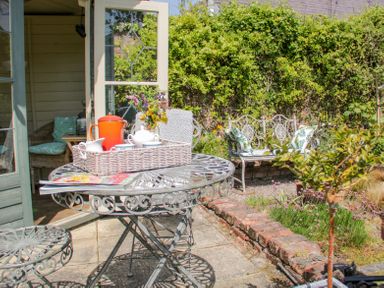 An outdoor patio with a metal table and chairs a tray with a teapot cups and flowers and a garden bench with cushions at Bryn Offa cottage in Holywell