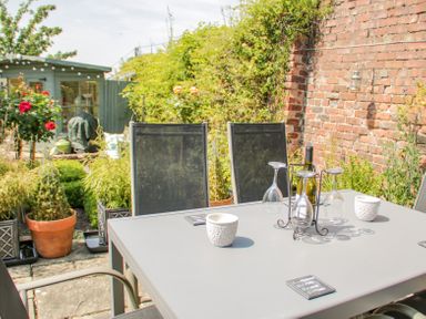 An outdoor patio with a table and chairs surrounded by plants and a brick wall at Bryn Offa cottage in Holywell