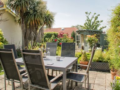An outdoor patio with a table and six chairs surrounded by plants and a small garden shed at Bryn Offa cottage in Holywell