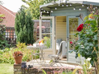 An outdoor garden area with a small round table and two chairs in front of a wooden summer house at Bryn Offa cottage in Holywell