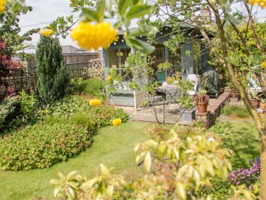 A garden with green grass plants a small patio with chairs and a table at Bryn Offa cottage in Holywell