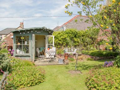 A garden with a small green shed a table and two chairs on a stone patio and various plants at Bryn Offa cottage in Holywell