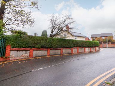 A road with a hedge and wall in front of a house at Bryn Offa cottage in Holywell