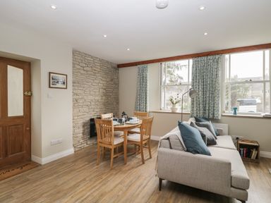 A dining area with wooden table and chairs next to a sofa with cushions by windows at The Old Haberdashery in Swanage