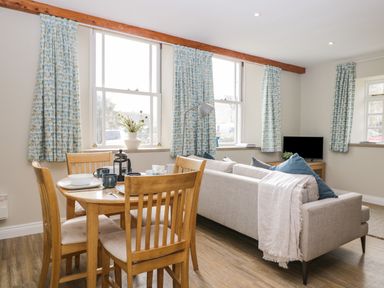 A dining table with four chairs next to a sofa and television in a living room at The Old Haberdashery in Swanage