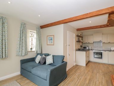 A living room with a blue sofa and patterned curtains next to a kitchen with white cabinets at The Old Haberdashery in Swanage