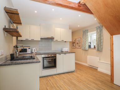 A kitchen with cabinets a stove microwave toaster kettle and a window with curtains at The Old Haberdashery in Swanage