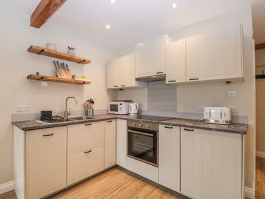A kitchen with white cabinets a stove a microwave a kettle a toaster and wooden shelves at The Old Haberdashery in Swanage