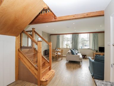 An open living room and dining area with wooden staircase and large windows at The Old Haberdashery in Swanage